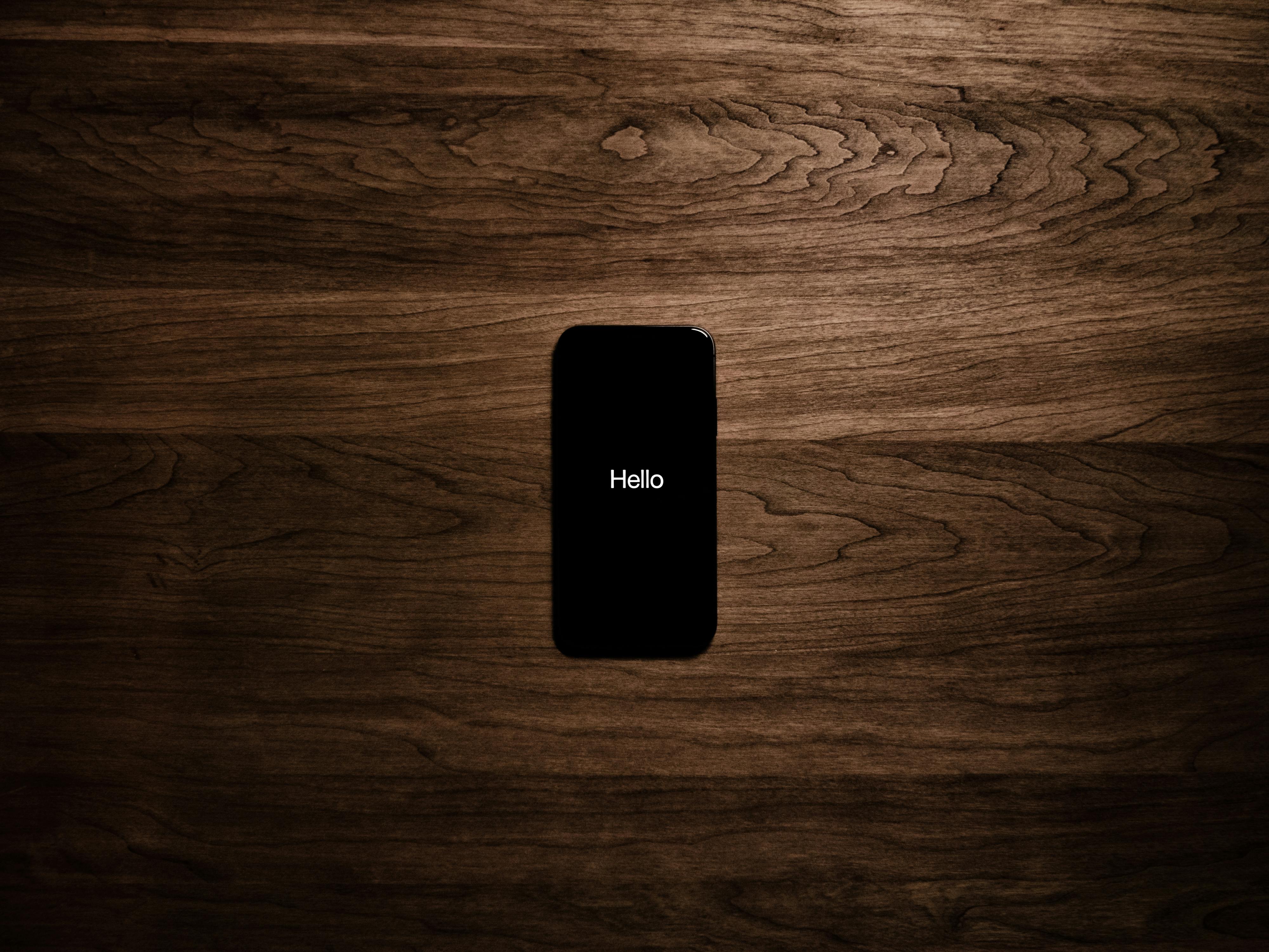 A smartphone displays 'Hello' against a dark wooden background, offering a sleek tech aesthetic.